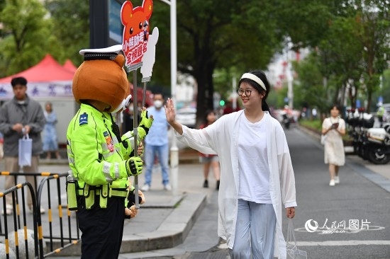 6月7日上午9時，隨著鈴聲的響起，2023年江西高考正式開考，江西省的53.57萬考生以縣（區(qū)）為單位隨機安排在全省256個考點、18968個考場參加高考。圖為“小熊交警”和考生擊掌鼓勵。 人民網(wǎng)記者 時雨攝