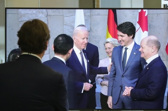 2022年3月24日，在比利時(shí)布魯塞爾的北約總部，一名男子觀看屏幕上美國(guó)總統(tǒng)拜登（右四）、歐盟委員會(huì)主席馮德萊恩（右三）、加拿大總理特魯多（右二）、德國(guó)總理朔爾茨（右一）出席七國(guó)集團(tuán)峰會(huì)合影儀式的畫(huà)面。新華社記者鄭煥松攝