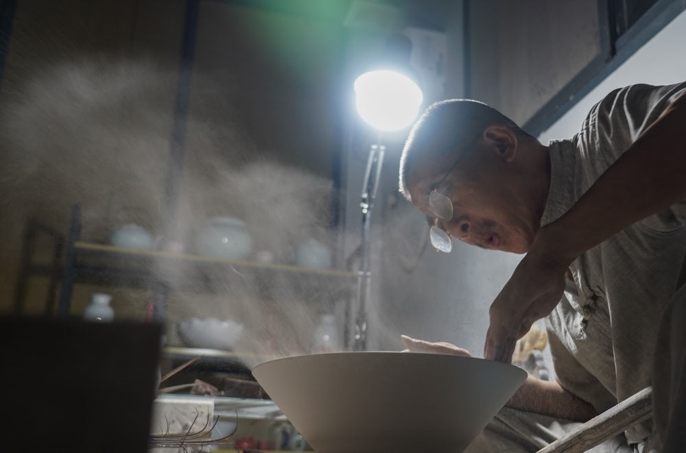 ↑ 在景德鎮(zhèn)，手工匠人吹去坯內(nèi)的泥土（2021年7月14日攝）。