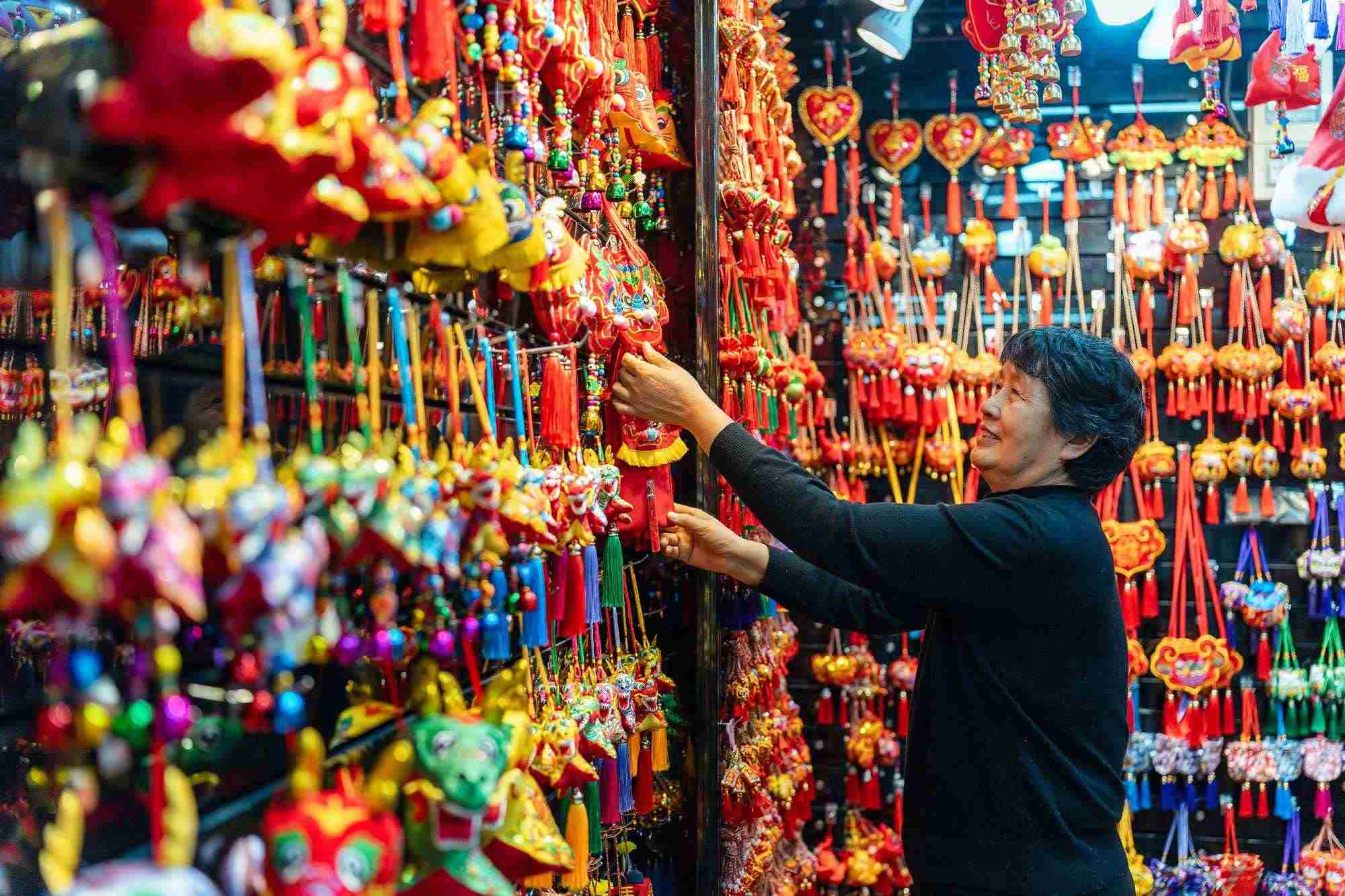 2023年12月11日，金華義烏國(guó)際商貿(mào)城，龍年喜慶用品掛滿攤位，顧客正在挑選中。