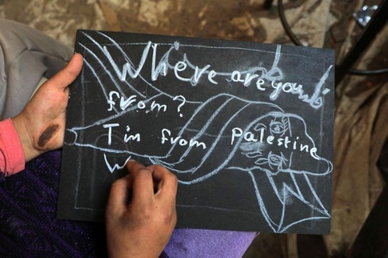 2023年12月28日，一名學生在加沙地帶南部城市拉法一所學校的臨時教室中寫下“我來自巴勒斯坦”的字樣。新華社發(fā)（里澤克·阿卜杜勒賈瓦德攝）