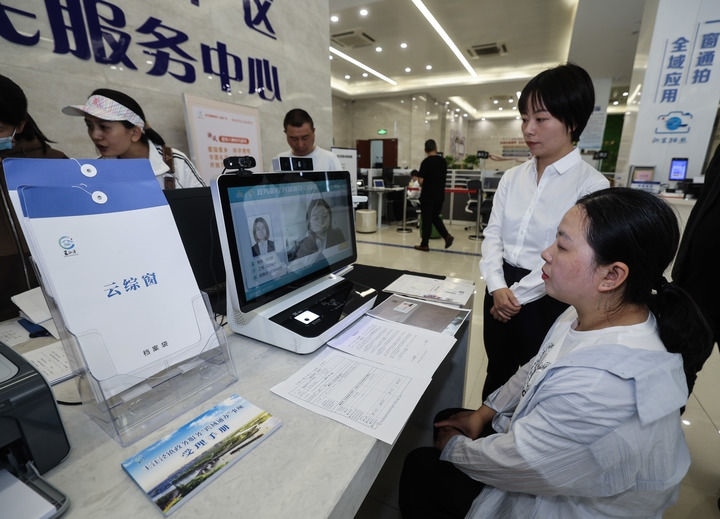 在浙江省嘉興市秀洲區(qū)王江涇鎮(zhèn)便民服務中心的“跨域通辦·云綜窗”窗口，辦理開業(yè)登記的個體工商戶（右一）通過該系統(tǒng)與江蘇省蘇州市吳江區(qū)盛澤鎮(zhèn)行政審批局工作人員視頻連線，進行身份讀取及材料線上審核（2024年5月9日攝）。新華社記者 徐昱 攝