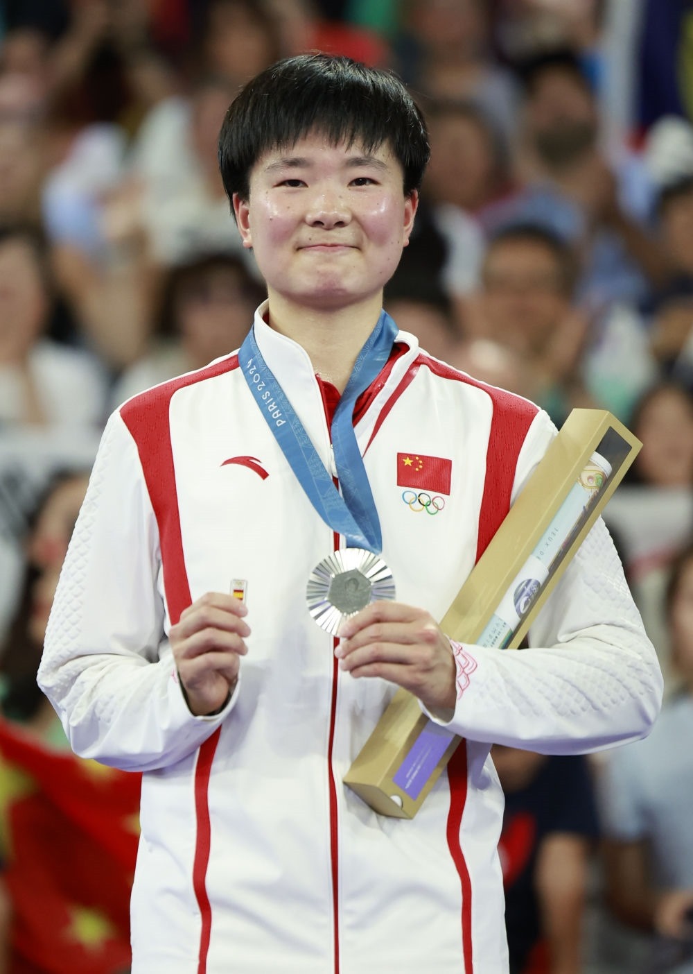 巴黎奧運(yùn)會(huì)羽毛球女子單打亞軍、中國(guó)選手何冰嬌在頒獎(jiǎng)儀式上一手握著銀牌，一手握著西班牙奧委會(huì)徽章（2024年8月5日攝）。新華社記者 任正來(lái) 攝