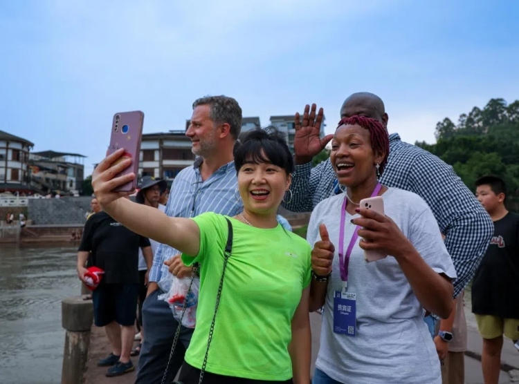 2024“一帶一路”媒體合作論壇聯(lián)合采訪調(diào)研行成員在樂山蘇稽古鎮(zhèn)與游客合影留念。本報(bào)記者 伊霄攝