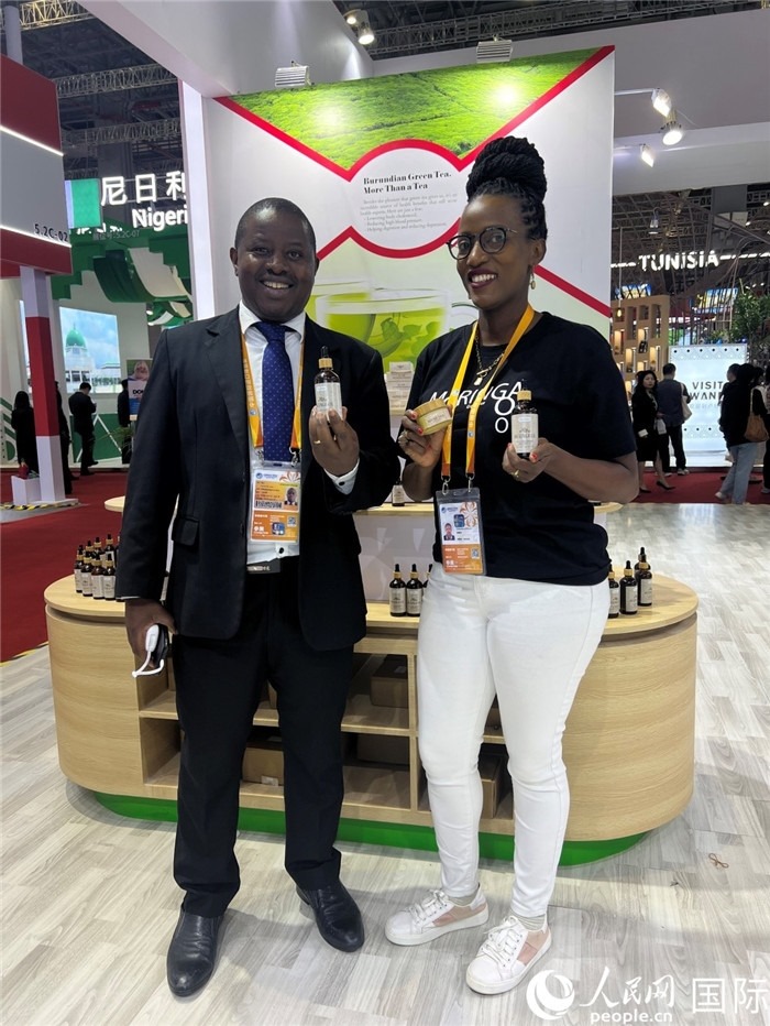 6月6日，布隆迪駐華大使館一等參贊布利馬索·阿爾弗雷德 (左，Bulimaso Alfred) 和參展商卡馬里扎·埃斯特拉 (Kamariza Estella) 在第七屆中國國際進(jìn)口博覽會布隆迪館展示當(dāng)?shù)厣a(chǎn)的辣木油。（人民網(wǎng) 艾里士 攝）