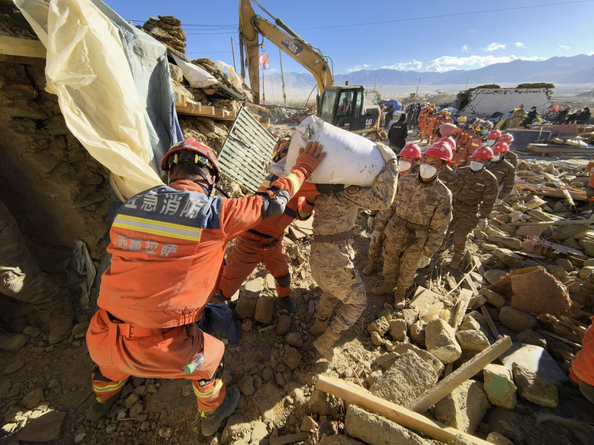 1月11日，定日縣長所鄉(xiāng)古榮村，應(yīng)急消防等救援人員排隊接力搶運掩埋在倒塌房屋下的群眾財物。人民日報記者楊翹楚攝