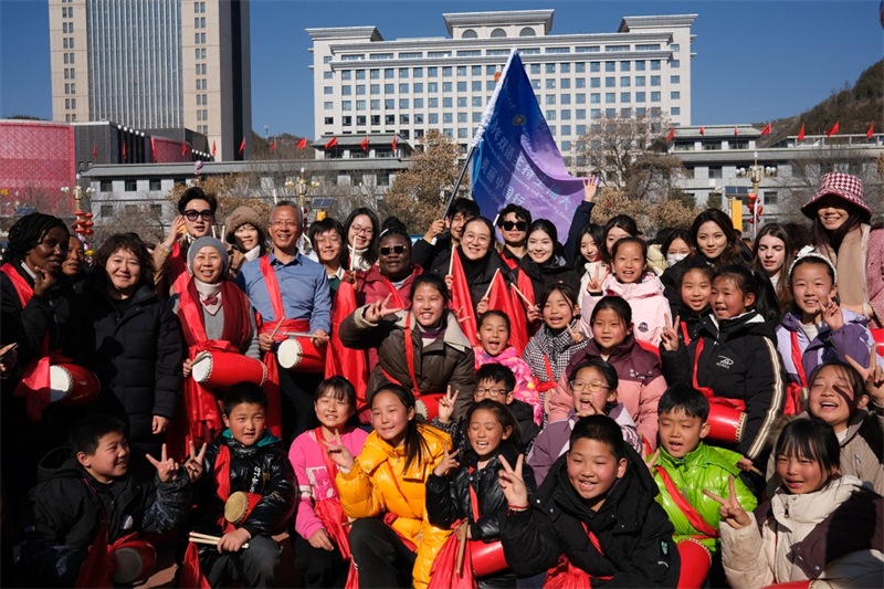 中外青年學(xué)子在安塞文化廣場觀看陜北腰鼓和大秧歌表演后合影留念，大家踏著鼓點(diǎn)共舞，翻飛的紅綢與躍動的身影交織，在黃土地廣場上繪出一幅生動的陜北民俗互動畫卷